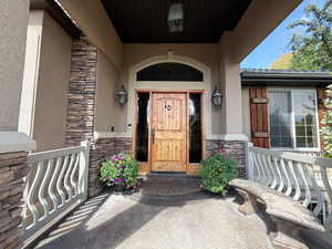 Property entrance with stone siding, stucco siding, and covered porch