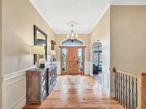 Entryway with a wainscoted wall, crown molding, a decorative wall, a chandelier, and light wood finished floors