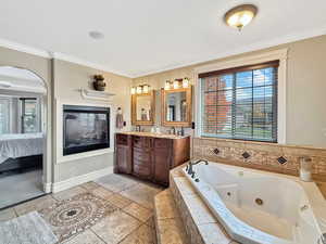 Full bathroom with a whirlpool tub, double vanity, connected bathroom, ornamental molding, and stone tile flooring