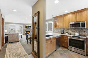 Kitchen featuring a warm lit fireplace, stainless steel appliances, backsplash, light stone counters, and glass insert cabinets