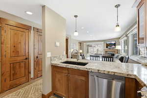 Kitchen with stainless steel dishwasher, a fireplace, brown cabinetry, hanging light fixtures, and recessed lighting