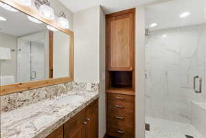 Bathroom featuring a marble finish shower, vanity, and recessed lighting