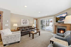 Carpeted living room featuring recessed lighting, a stone fireplace, and a sliding door to the patio
