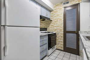 Kitchen featuring freestanding refrigerator, gas stove, light tile patterned floors, under cabinet range hood, and gray cabinetry