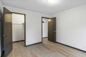 Unfurnished bedroom with a spacious closet, a textured ceiling, and light wood-style floors