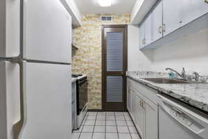 Kitchen with white appliances, light stone countertops, and light tile patterned floors