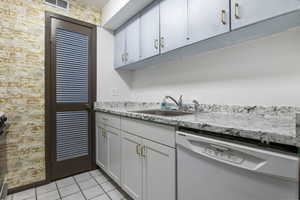 Kitchen with dishwasher, brick wall, light tile patterned floors, and stainless steel range oven