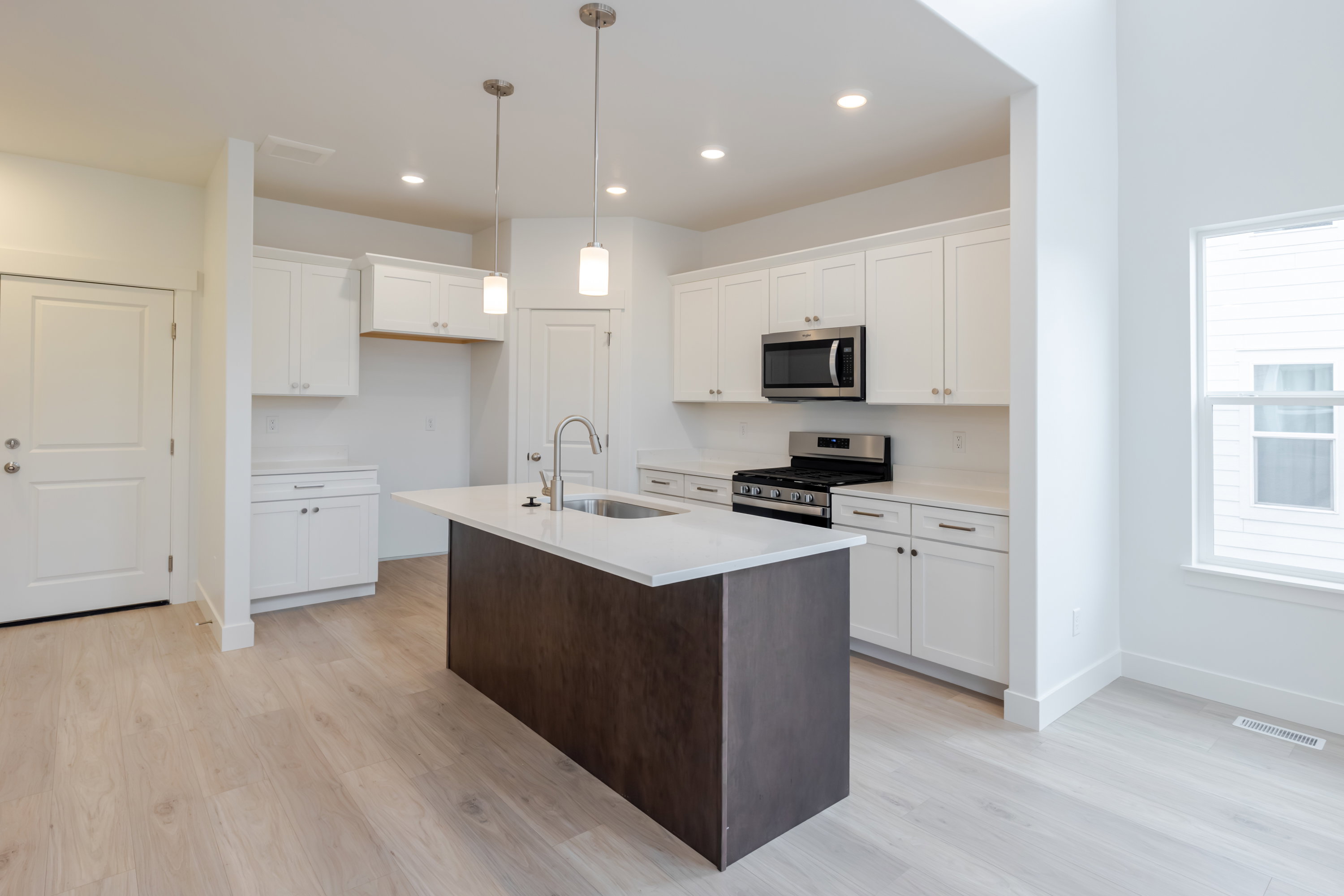 Kitchen featuring a dark wood-finish island with a white countertop and undermount sink, white cabinetry, stainless steel microwave, gas range, and wood-finish flooring