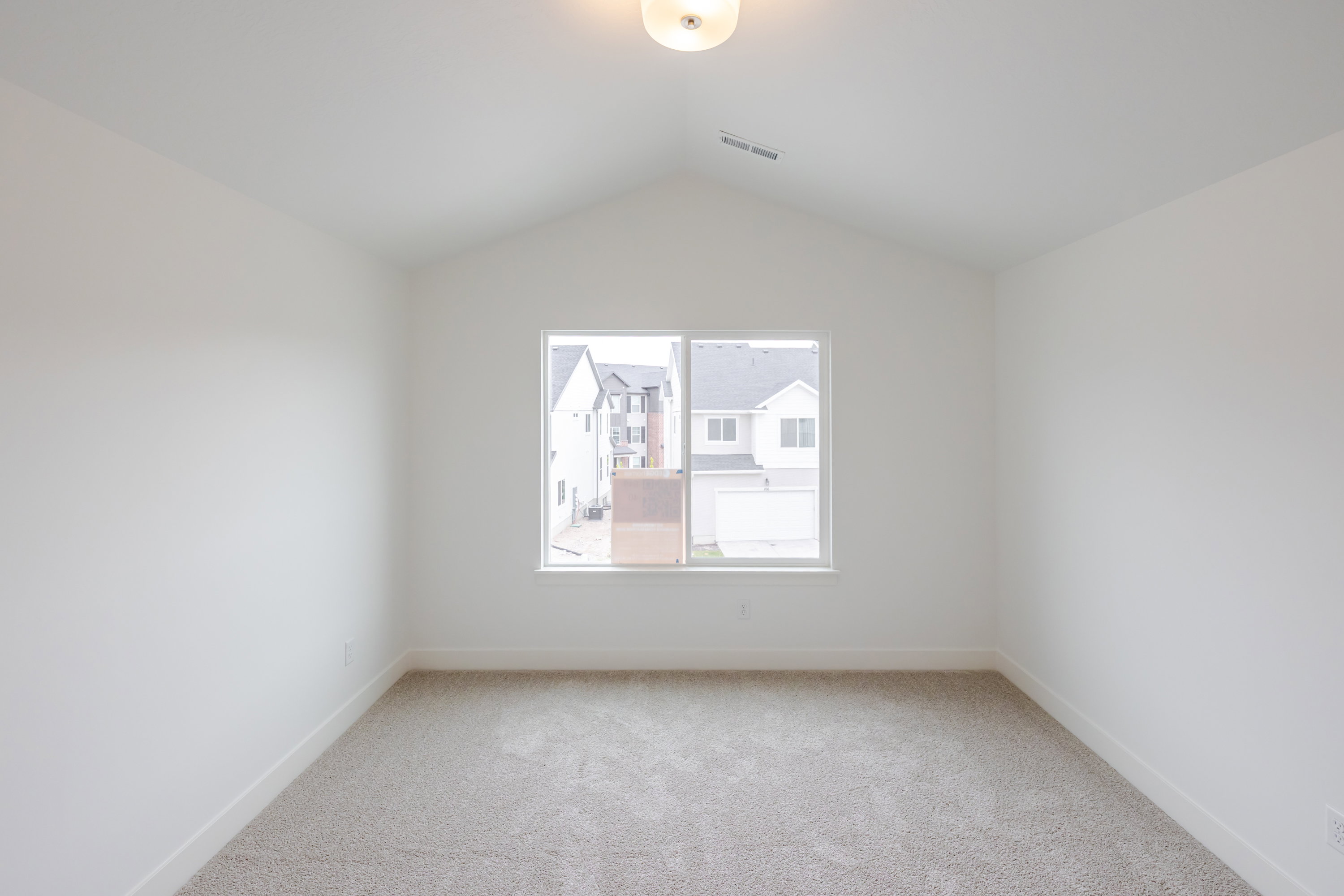 Vaulted ceiling room featuring a large window, neutral carpeting, and white baseboards