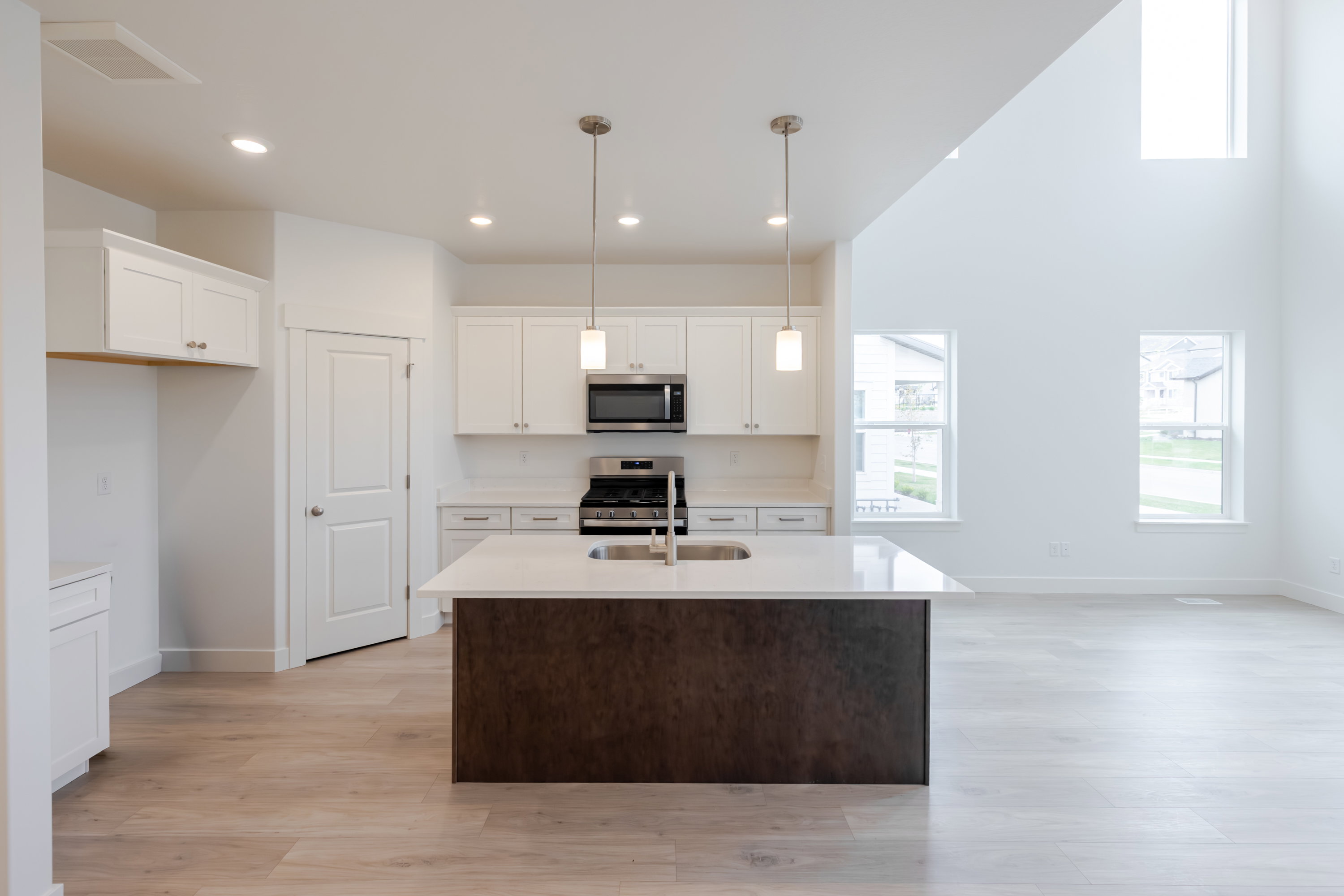 Open-concept kitchen featuring an island with a built-in sink, stainless steel appliances, white cabinetry, and light wood-finish flooring
