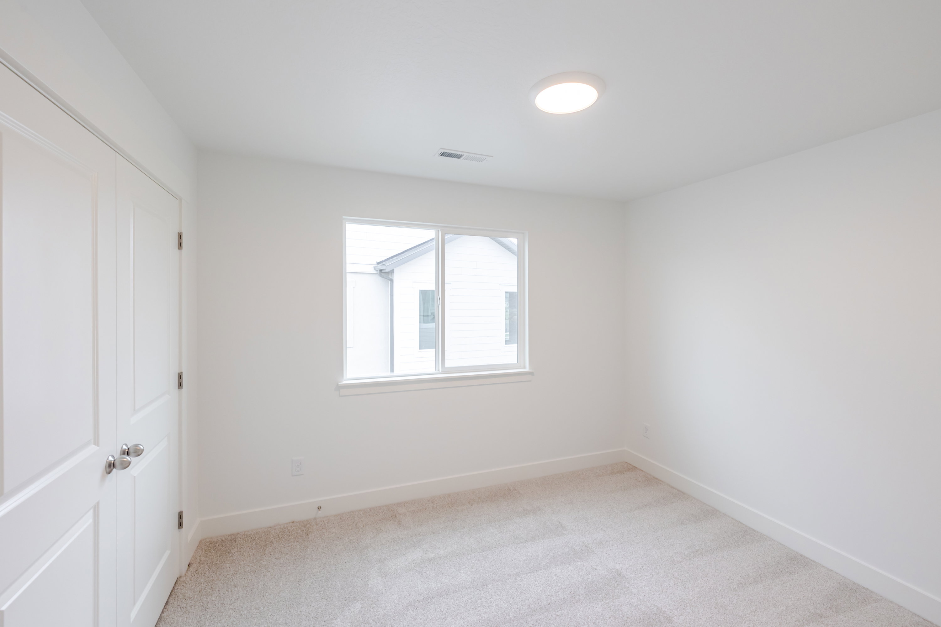 Bright interior space featuring a window, light-toned carpeting, white walls, and a flush-mount ceiling light fixture
