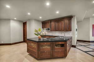 Bar area with dark brown cabinetry, recessed lighting, dark stone countertops, and stainless steel microwave