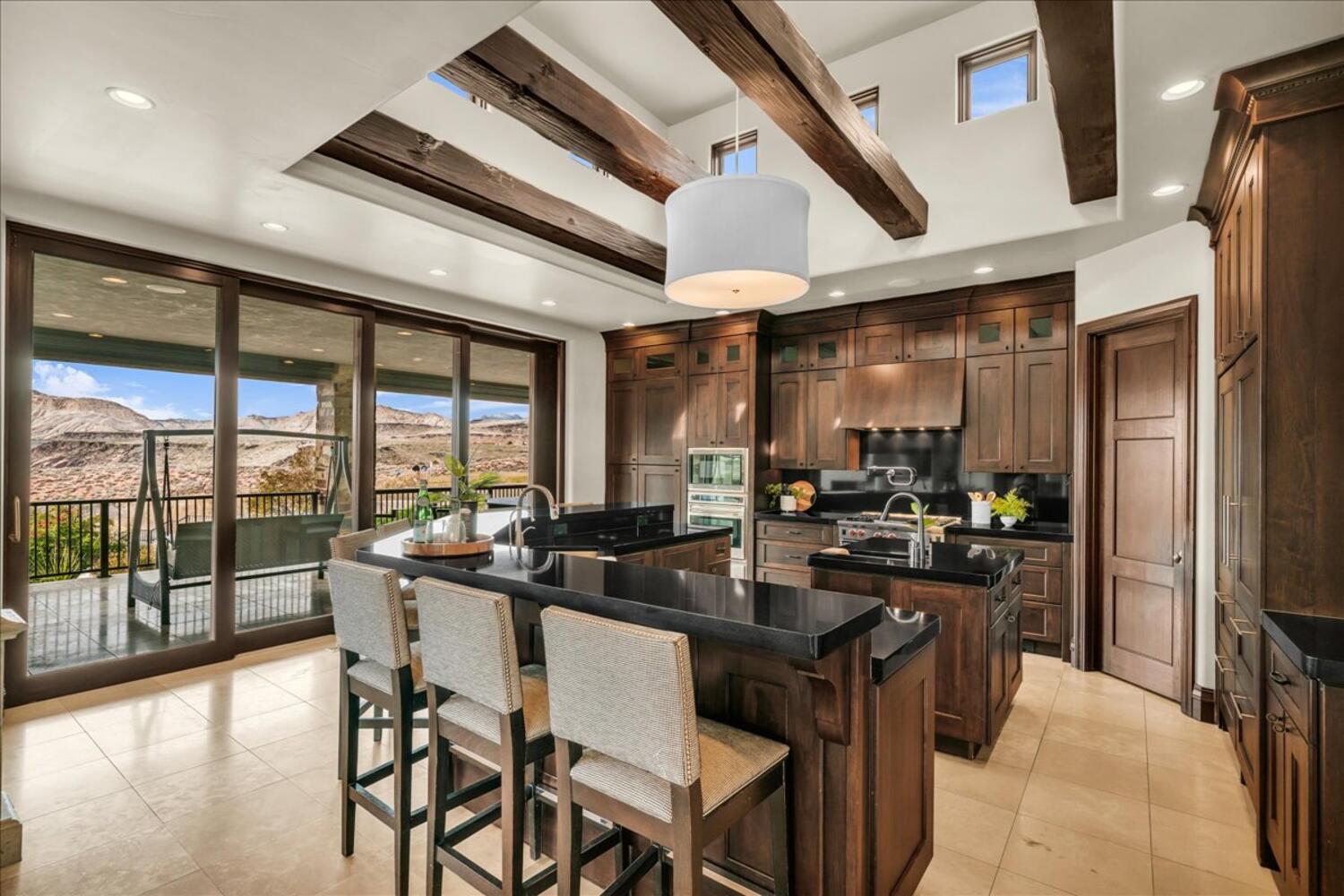 Kitchen featuring a breakfast bar, pendant lighting, beam ceiling, stainless steel appliances, and under cabinet range hood