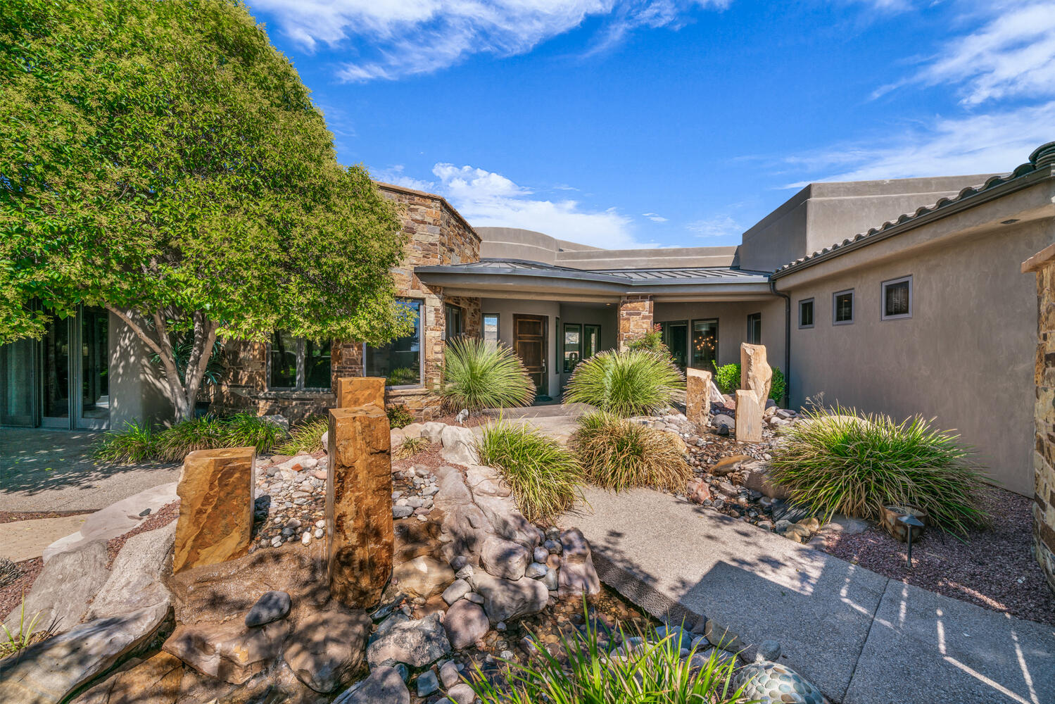 View of front of property with stone siding, a patio, stucco siding, and a metal roof