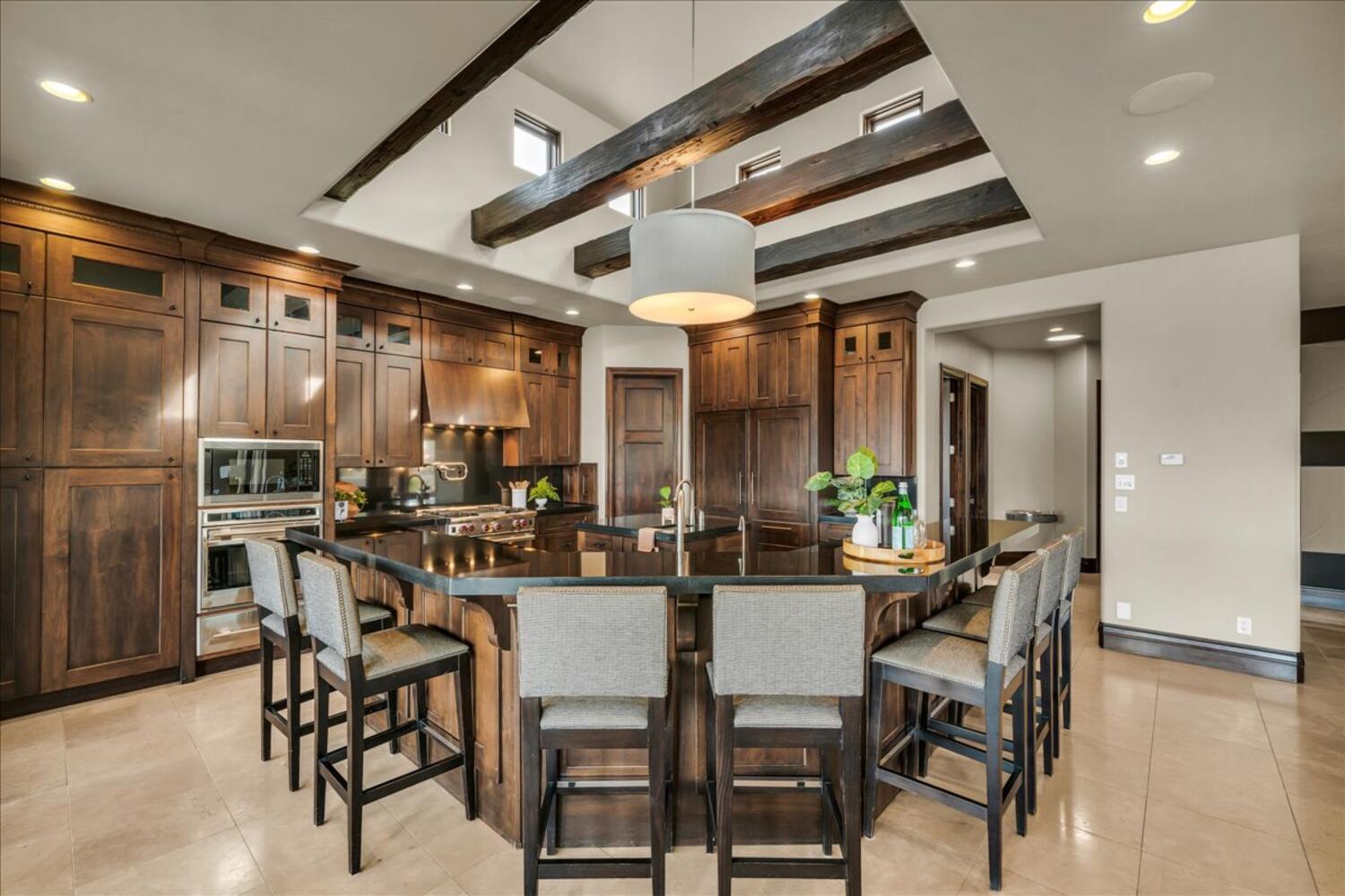 Kitchen featuring a breakfast bar area, glass insert cabinets, oven, decorative light fixtures, and beam ceiling
