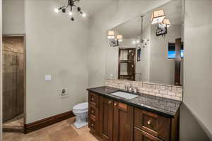 Bathroom featuring vanity, a tile shower, a chandelier, and tasteful backsplash