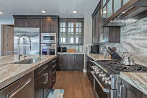 Kitchen featuring dark brown cabinetry, built in appliances, glass insert cabinets, exhaust hood, and recessed lighting