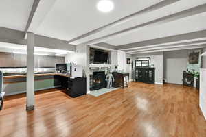 Living room featuring a stone fireplace, light wood-style floors, beam ceiling, and a desk