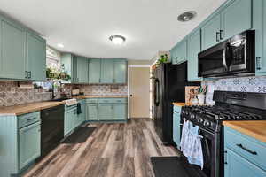 Kitchen with black appliances, butcher block counters, dark wood-style flooring, a textured ceiling, and green cabinets