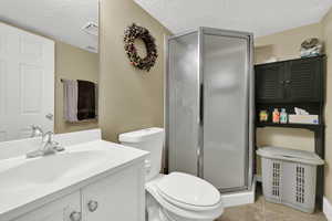 Full bath featuring a textured ceiling, vanity, a stall shower, light tile patterned floors, and a textured wall