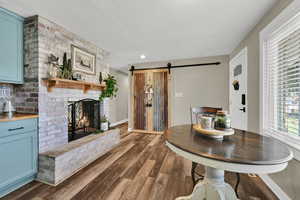 Dining space with a barn door, dark wood-style flooring, a brick fireplace, and a textured ceiling