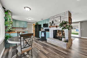 Kitchen featuring green cabinets, black appliances, a brick fireplace, decorative backsplash, and a textured ceiling