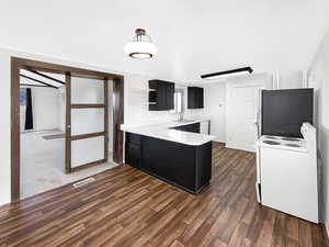 Kitchen featuring dark cabinets, light countertops, white electric range oven, a peninsula, and open shelves