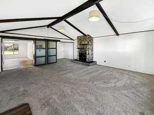 Unfurnished living room with a barn door, carpet floors, and a stone fireplace
