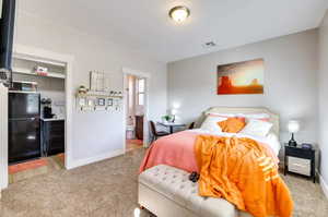 Bedroom featuring light colored carpet, freestanding refrigerator, and ensuite bath