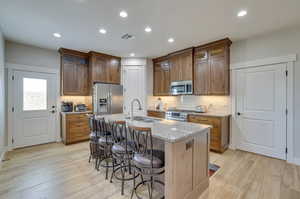 Kitchen featuring light stone counters, a kitchen bar, stainless steel appliances, a center island with sink, and light wood-style flooring