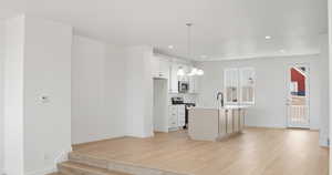 Kitchen featuring hanging light fixtures, appliances with stainless steel finishes, a chandelier, white cabinets, and light wood-style flooring