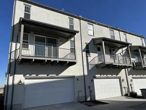 Rear view of property with stucco siding, an attached garage, and a balcony
