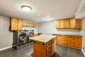 Laundry area featuring a textured ceiling, independent washer and dryer, cabinet space, and dark tile patterned flooring