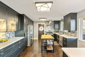Kitchen featuring backsplash, light stone counters, wall chimney range hood, and appliances with stainless steel finishes