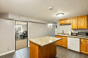 Kitchen featuring a textured ceiling, white dishwasher, a kitchen island, light stone countertops, and stainless steel microwave
