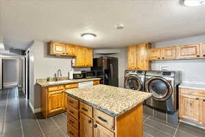Kitchen featuring washer and dryer, a kitchen island, a textured ceiling, black refrigerator with ice dispenser, and dark tile patterned flooring