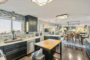 Kitchen with decorative light fixtures, light stone countertops, stainless steel dishwasher, and dark wood-style flooring