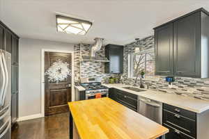 Kitchen featuring butcher block countertops, appliances with stainless steel finishes, wall chimney range hood, dark wood-style flooring, and tasteful backsplash