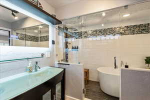 Full bathroom with a freestanding bath, vanity, a textured wall, dark tile patterned flooring, and a stall shower