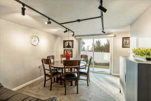 Dining space with rail lighting, a textured ceiling, and light colored carpet