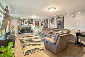 Carpeted living room with rail lighting, a textured ceiling, and a brick fireplace