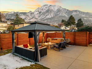 Patio terrace at dusk featuring an outdoor living space with a fire pit, a fenced backyard, a gazebo, a patio area, and a mountain view