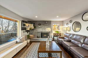 Living area featuring dark wood-type flooring, a stone fireplace, and recessed lighting