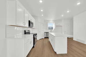 Kitchen featuring stainless steel appliances, white cabinetry, decorative backsplash, light wood-type flooring, and recessed lighting