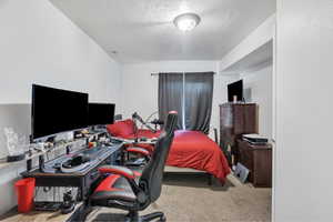 Bedroom with an office area, a textured ceiling, light carpet, and a textured wall
