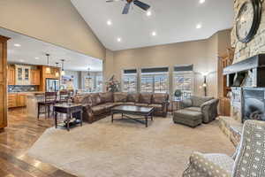 Living area with recessed lighting, high vaulted ceiling, a stone fireplace, light wood finished floors, and a ceiling fan