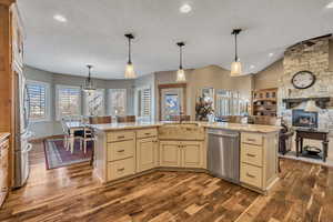 Kitchen featuring pendant lighting, cream cabinets, light stone counters, appliances with stainless steel finishes, and a textured ceiling