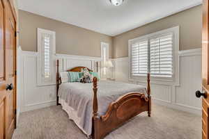 Bedroom with wainscoting, multiple windows, light colored carpet, and a decorative wall