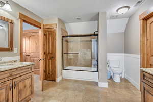 Bathroom with vanity, enclosed tub / shower combo, a wainscoted wall, a textured ceiling, and lofted ceiling