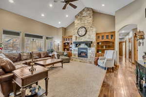 Living area with high vaulted ceiling, a stone fireplace, hardwood / wood-style flooring, arched walkways, and ceiling fan